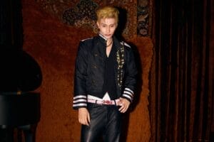 Promotional image which sees BENZO, with blond hair, dressed in black, in a swagger stance, looking slightly down at the camera. There's also a piano on the left.