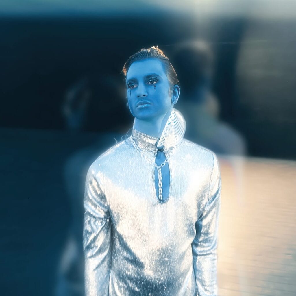 Exclusive Premiere: Aurelia & Icarus Moth Team Up with Ehiorobo on Mesmerising New Single and Visual Titled “SUPERNOVA” 11 Still from the "SUPERNOVA" music video which shows Icarus Moth bathed in blue light, wearing a silver outfit.
