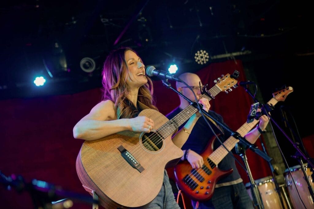 Meg Whalen performing on stage with her guitar and a microphone in front of her.