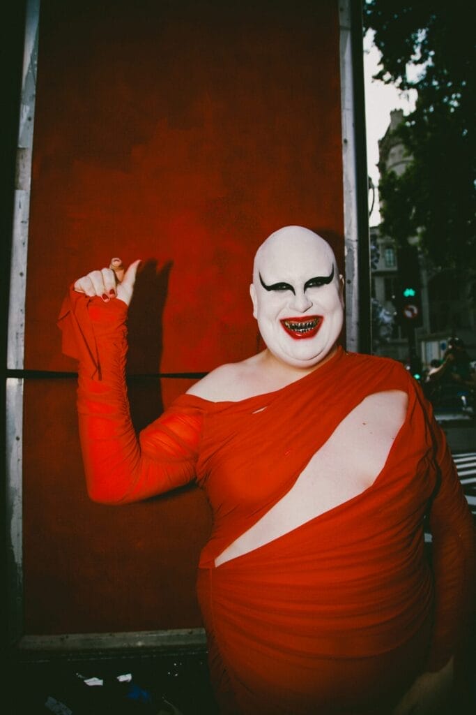 Lewis G. Burton wearing white make-up with red lips that matches the colour of their red dress.