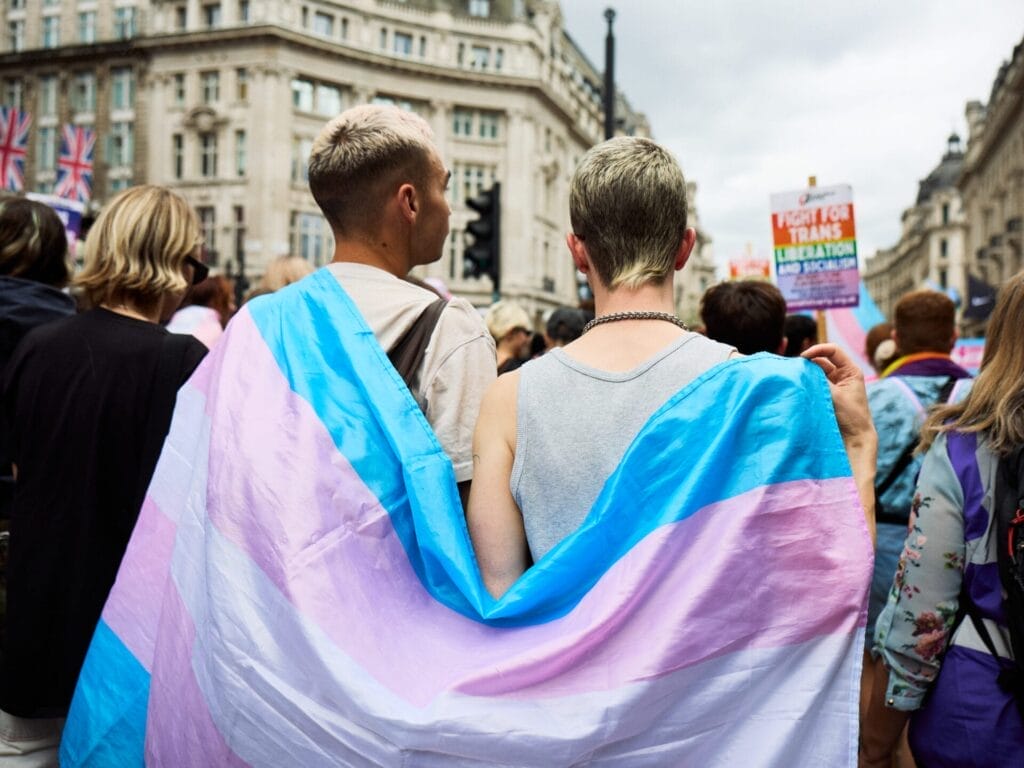 Two men holding a trans flag together, around their shoulders, as part of the London Trans+ Pride 2025.