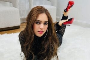 Cropped photo of the official single cover artwork for "Good For A Minute", which sees Camille K wearing a black lace outfit and a pair of Louboutin heels. She's lying on her stomach with her knees bent and the heels in the air, leaning on her elbows with her hands out in front of her. The hardwood floor is covered by a grey-white rug which she is lying on.