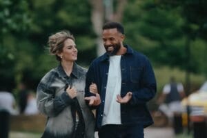 Screenshot from the "In It With You" music video which sees JoJo on the left and Craig David on the right, walking in a park together with their arms linked, talking.