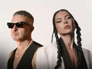 MoBlack and INNA posing in an edited photo which has cropped the two of them and put them together in an image. MoBlack is looking to the left, wearing shades, whereas INNA is on the right with her make-up on-point and her hair in two braids coming down her face on each side and falling past her shoulders.