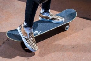 Close-up of someone wearing the cardboard Vans Slip-On sneakers standing on a skateboard.