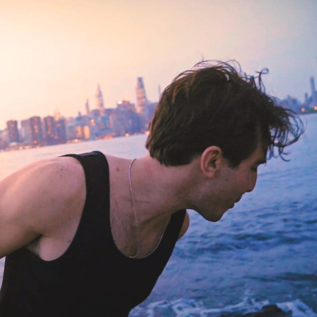 Official single cover artwork for "Pretty Long Island Girls" which sees Brett Altman looking away from the camera, wearing a black vest. Behind him is a city in the background with a large mass of water, which might well be the Hudson river, referenced in the song, and he's looking out at the surf.