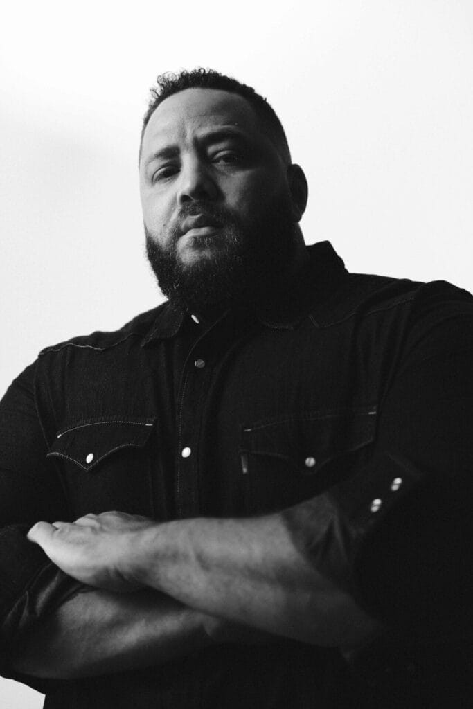 Official press photo which shows a black-and-white image of Daddyphatsnaps posinng with his arms crossed and wearing a dark shirt.