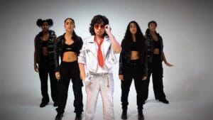 Still from the official music video for "Baile" which sees Nico Rocks wearing silver trousers and a matching jacket alongside a red tie and red shades, reminding us of Elvis, getting ready to knock out choreography to the track with his four backing dancers.