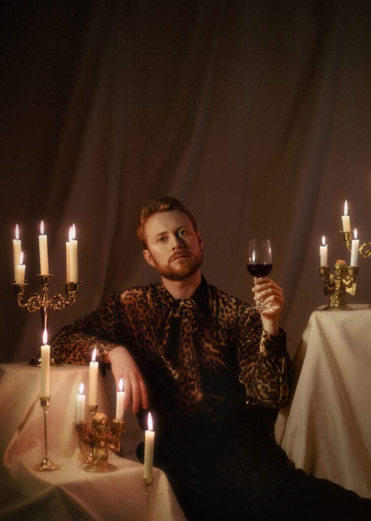 John Tothill relaxing with a glass of red wine, lit by candlelight as candles appear on tables surrounding him.