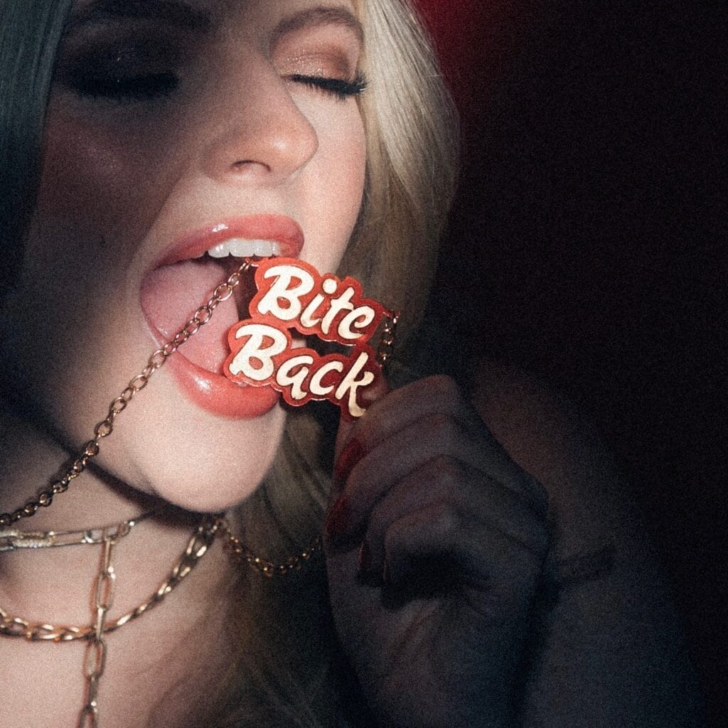Official single cover artwork for "Bite Back" which sees Remy Garrison biting a necklace that has the song's title on it. The necklace is spotlighted while the rest of her is shadowed.