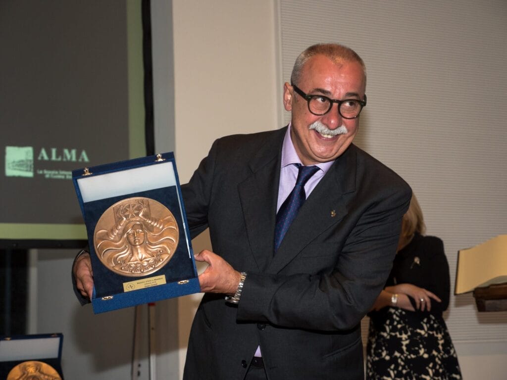 Sergio Dondoli holding up a medal award that he won while wearing a suit.