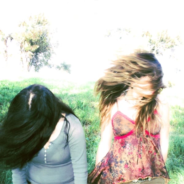 Official single cover artwork for Hailey Hermida's "straitjacket" which sees two women with their hair covering their faces, standing in a park with grass and trees behind them.