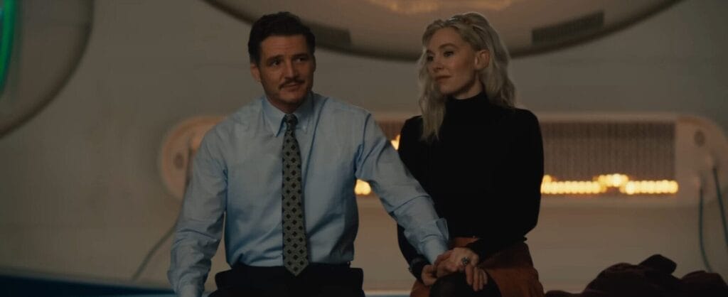 Still from the official trailer of The Fantastic Four: First Steps, which sees Reed Richards and Sue Storm sitting next to one another with Richards putting a hand on Storm's leg to comfort her. He is wearing a suit and tie, while she's wearing a black jumper and a brown skirt with black tights.