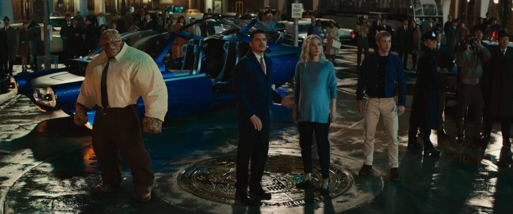 Still from the official trailer to The Fantastic Four: First Steps film where all four main characters are stood in Times Square with the blue Fantastic Four car behind them. It is night-time and they're wearing civilian clothes.