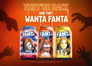 Three Halloween-themed cans of Fanta displaying Chucky, Freddy Fazbear, and M3gan, with an orange background with shadowy hands grabbing for the cans in each corner. At the top in white text are the words, "They're back and they wanta Fanta."