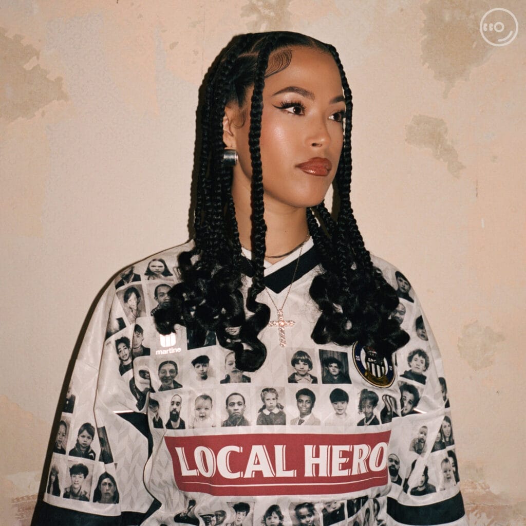 Official single cover artwork for "Hypnotic" which sees Jazzy facing slightly to the right and wearing a t-shirt that has a bunch of face portraits on it with the words "Local Hero".