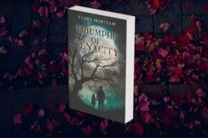 Paperback novel of Yusra Mariyam's book "Triumphs of Tenacity" which shows a dark tree and two shadowy figures hand-in-hand walking to a bright full moon. The book is placed in front of a background of red leaves.