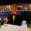 Kane Crookes wearing a suit and bowtie with a graduation gown, smiling, while sitting at a table.