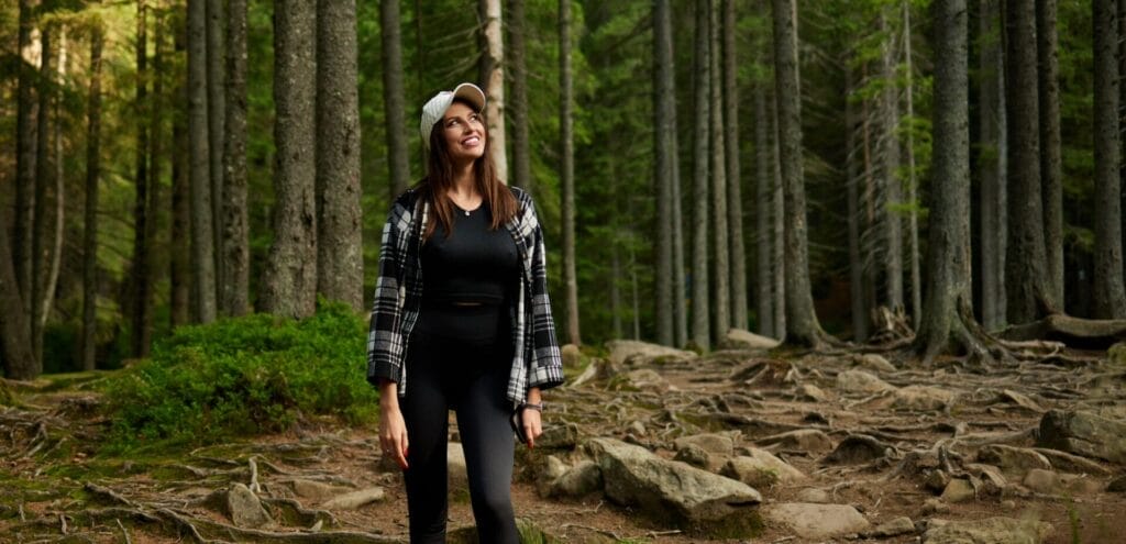 Ukrainian Singer ZHANNET on Viral Success of “Women’s Happiness” Duet With Ivo Bobul and Her TikTok Transformation 21 ZHANNET wearing casual attire and a cap smiling while walking through a serene forest, with tall trees and exposed roots. The mood is peaceful and reflective.