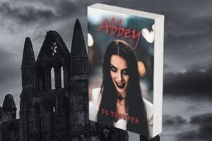 A book titled "Abbey" by TG Trouper with a vampire woman on the cover, set against a dramatic, dark sky and a gothic-style, Whitby Abbey.