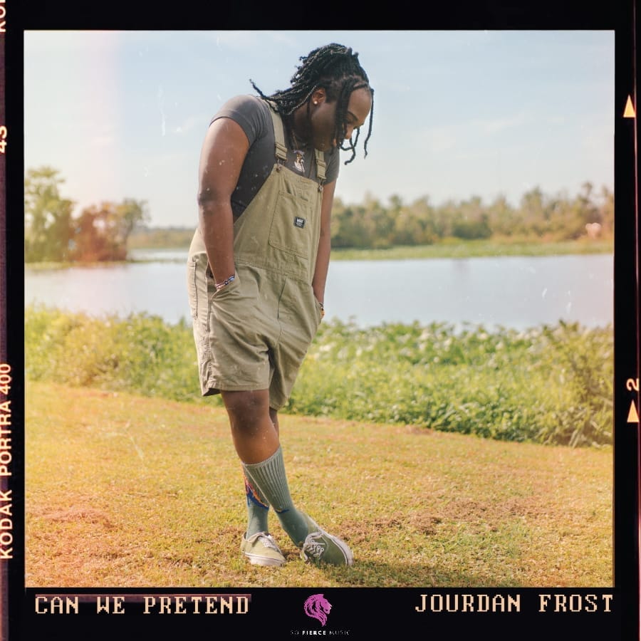 Official single cover artwork for "Can We Pretend" which shows Jourdan Frost in green overalls standing pensively by a lake under a clear sky, surrounded by greenery. The warm tones convey a calm, reflective mood.