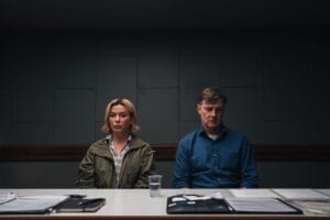 Photo from Gone the ITV commissioned TV series which shows Eve Myles in a green jacket and David Morrissey in a blue shirt sitting at a table with documents and a glass of water, looking serious against a dark background.