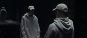 Still from the "FEAR" music video which shows NF in a white hoodie and cap facing a mirror, creating a reflective scene. The dim lighting conveys a somber, introspective mood.