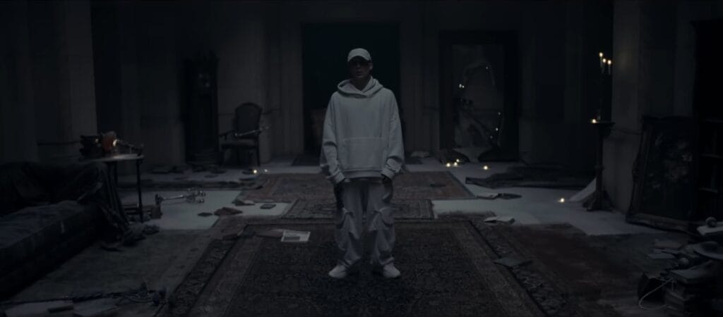 EP Review: NF’s “FEAR” Explores a Raw and Vulnerable New Chapter With mgk and James Arthur 41 Still from the "FEAR" music video which shows NF in a white hoodie and cap standing in the centre of a dimly lit, cluttered room. The space is filled with scattered papers, furniture, and an eerie ambiance.