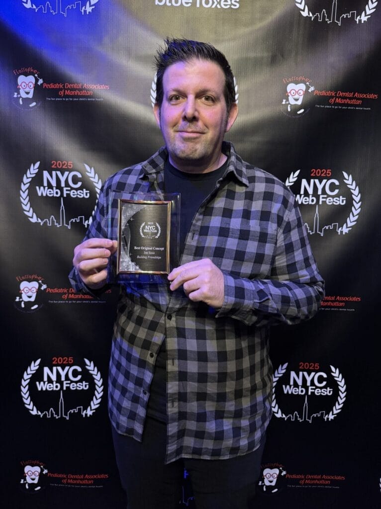 Jon Sosis dressed in a plaid shirt proudly holding an award plaque at the 2025 NYC Web Fest. The event's logo and laurels are displayed prominently behind him.