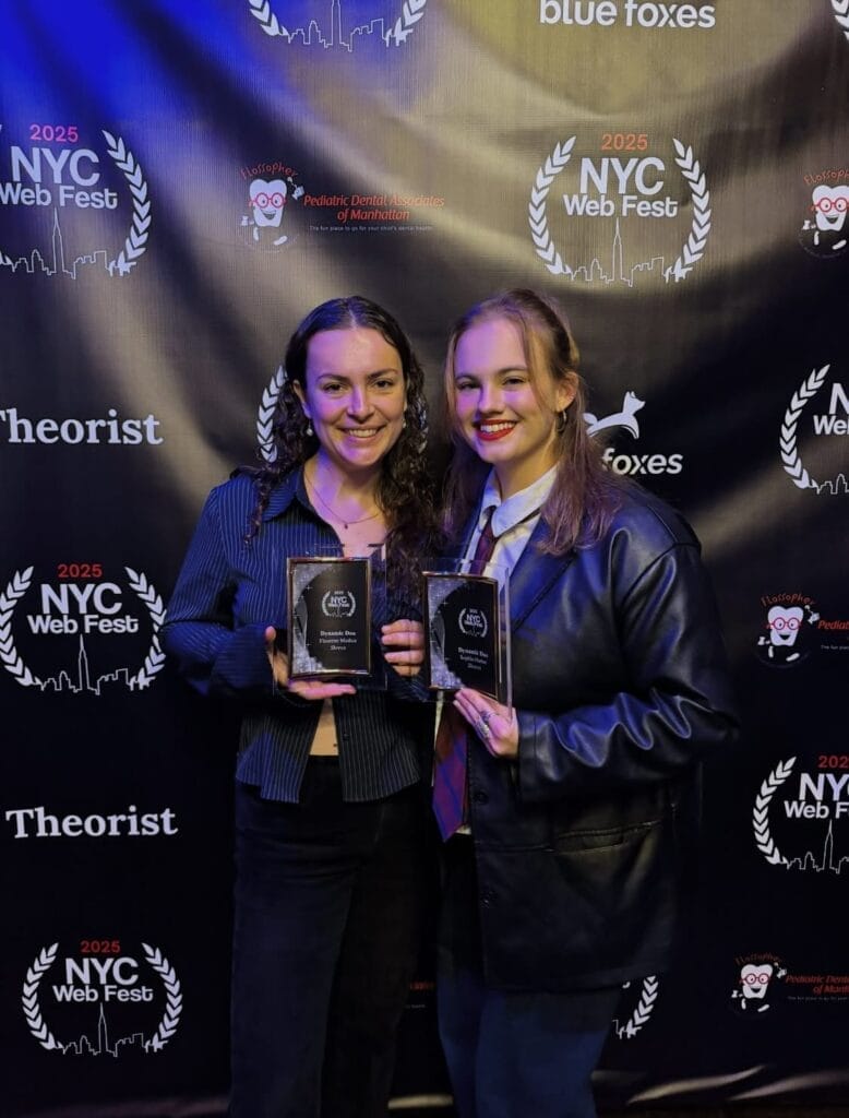 Sophia Harber & Fleurette Modica smiling and holding awards at the 2025 NYC Web Fest. They stand in front of a branded backdrop, conveying excitement and pride.