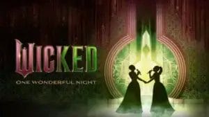 Title card for "Wicked: One Wonderful Night" with two silhouetted women, presumedly Glinda and Elphaba, facing each other, holding hands, against a backdrop of bright green and intricate patterns.