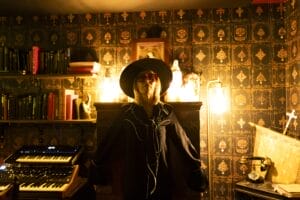 Janie Price (Bird), posing in a black blouse, a big rimmed black hat and some shades, in the middle of a recording studio.